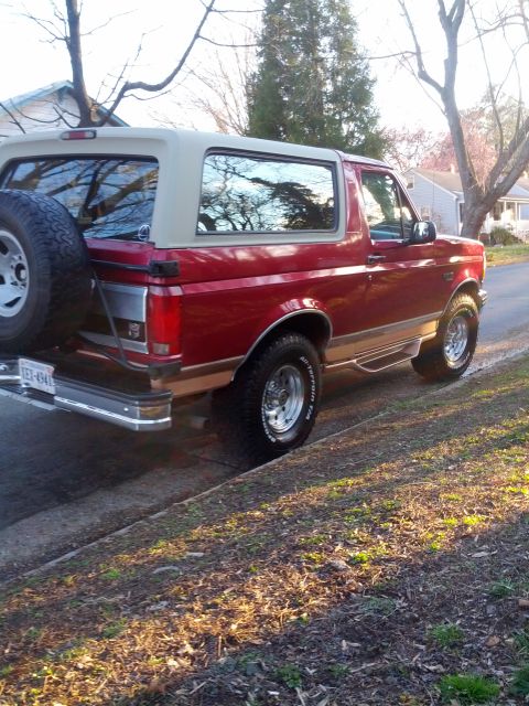 1995 Ford Bronco - This red Ford Bronco with a tan top is parked on the side of a residential street.