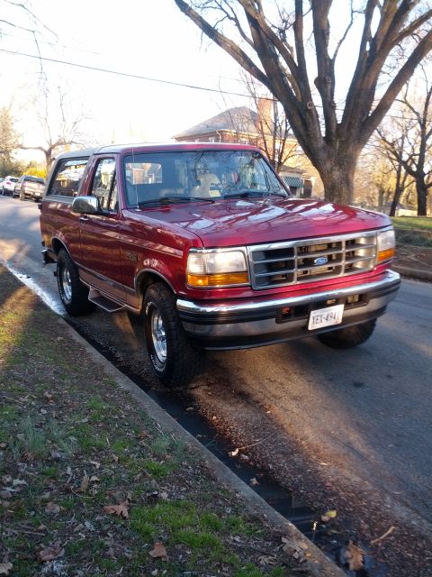 1995 Ford Bronco - This red 1995 Ford Bronco is parked on the side of a street, showing its front quarter profile.