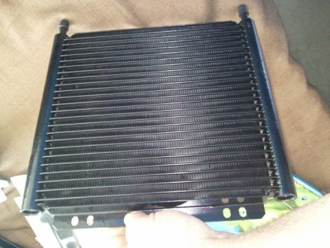 1994 Ford Bronco - A black transmission cooler part is held by a hand, with a Supermotors.net logo visible at the bottom.