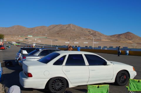 1995 Ford Taurus - White 1995 Ford Taurus parked at a racetrack with mountains in the distance.