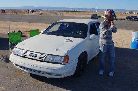 1995 Ford Taurus - A white 1995 Ford Taurus, modified for racing, sits on a track with a person in racing gear nearby.