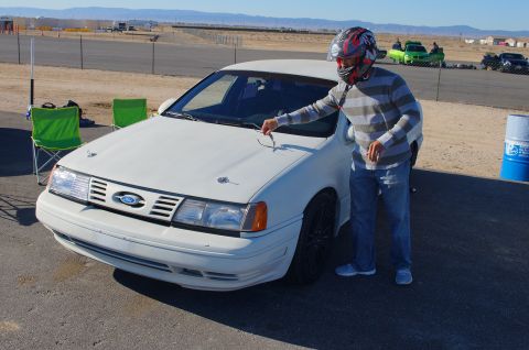 1995 Ford Taurus - Man in helmet by a white 1995 Ford Taurus at a track.