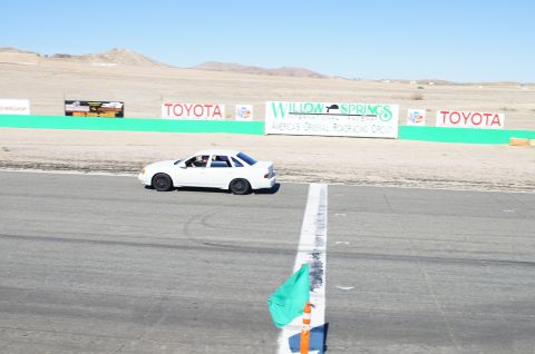 1995 Ford Taurus - A white sedan drives on the asphalt of Willow Springs International Raceway, with sponsor signs visible on the trackside.