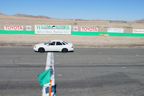 1995 Ford Taurus - A white sedan is on the track at Willow Springs International Raceway, with sponsor signs visible.