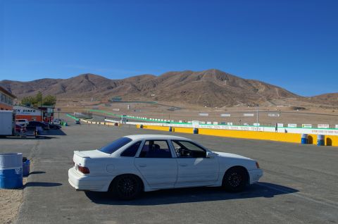 1995 Ford Taurus - White 1995 Ford Taurus parked on asphalt at a racetrack with mountains in the background.