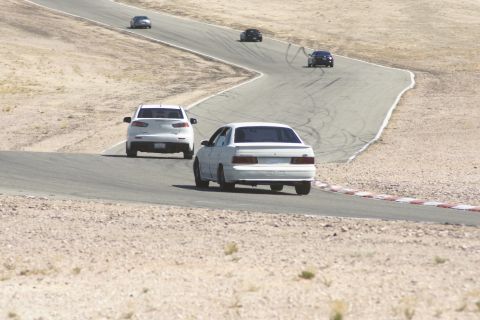 1995 Ford Taurus - A white 1995 Ford Taurus sedan navigates a turn on a desert race track with other vehicles present.