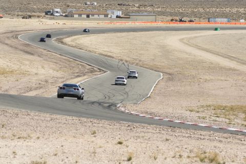 1995 Ford Taurus - A silver sports car navigates a curve on a desert race track, with several other vehicles following behind.