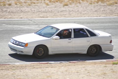1995 Ford Taurus - 1995 Ford Taurus sedan on a race track, driver visible with helmet.