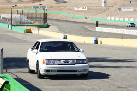 1995 Ford Taurus - A white sedan drives on a race track with various sponsor signs visible in the background.