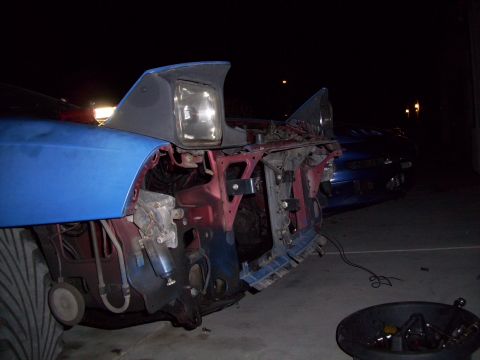 1995 Ford Probe - The front of a blue car is disassembled, revealing its internal components and headlights, with another vehicle in the background.