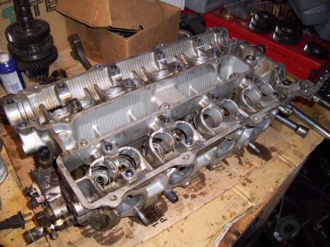 1995 Ford Probe - Disassembled engine cylinder head sits on a cardboard surface, surrounded by various automotive parts and tools.