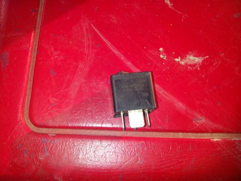 1979 Ford Bronco - A black electrical relay with metal prongs is shown against a red textured background.