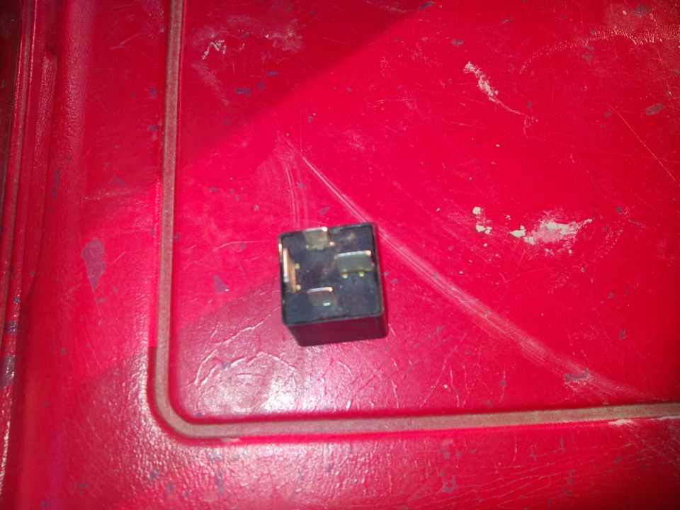 Black automotive relay with metal prongs on a red textured surface