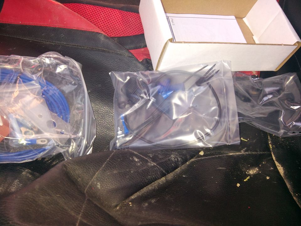 Parts in plastic bags on black and red car seats. A white box is open in the background