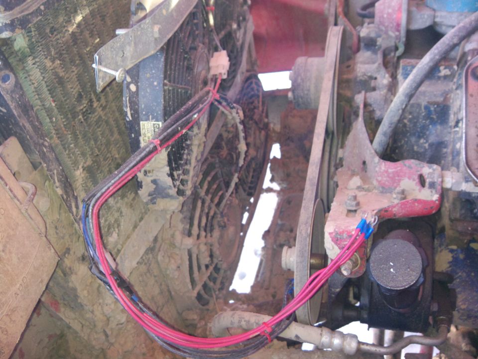 Engine bay showing two electric fans, wiring, and a belt pulley system. Mud covers many components