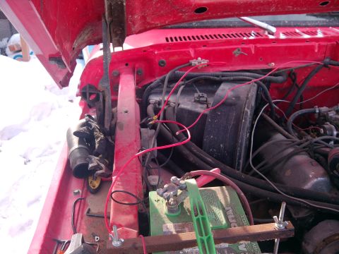 1979 Ford Bronco - The engine bay of a red vehicle shows a battery and various wires, with a pair of gloves nearby.