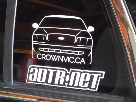 2003 Ford Crown Victoria - Close view of white CrownVic.ca front-end outline decal above an ADTR.net logo sticker on a tinted window