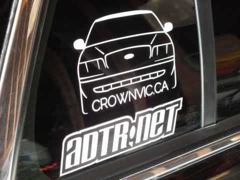 2003 Ford Crown Victoria - Vinyl CrownVic.ca sedan-front decal sits above the ADTR.net logo sticker on a dark tinted vehicle window