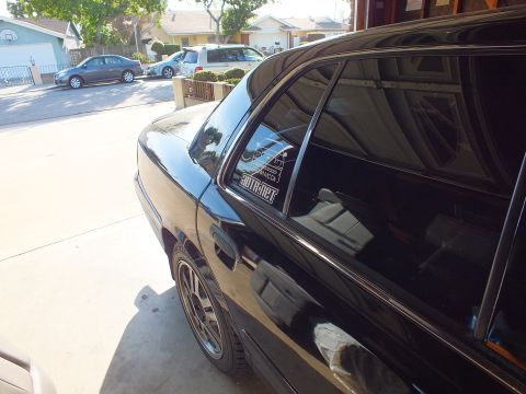 2003 Ford Crown Victoria - Black sedan rear quarter and alloy wheel in a sunny driveway, CrownVic.ca and ADTR.net decals on the window