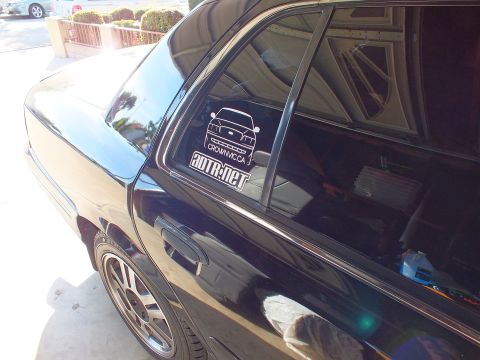 2003 Ford Crown Victoria - Black sedan rear side panel and chrome alloy wheel under a carport, CrownVic.ca and ADTR.net decals on glass