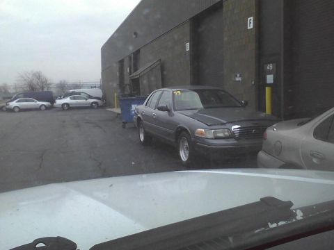 2003 Ford Crown Victoria - A 2003 Ford Crown Victoria is parked outside a commercial building, with other vehicles visible in the background.