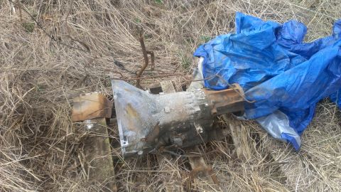 1995 Ford Bronco - A transmission part rests on a wooden pallet amidst dry grass and is partially covered by a blue tarp.