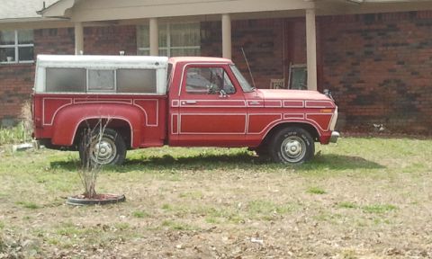 1987 Ford Bronco - A red pickup truck with a white camper shell is parked on a grassy area in front of a brick house.