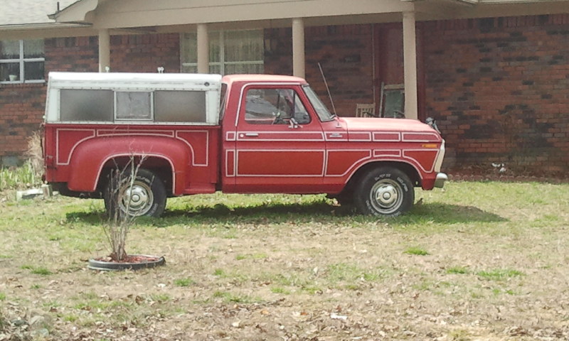 Red pickup truck with white camper shell, side view, showing decorative trim and chrome bumper