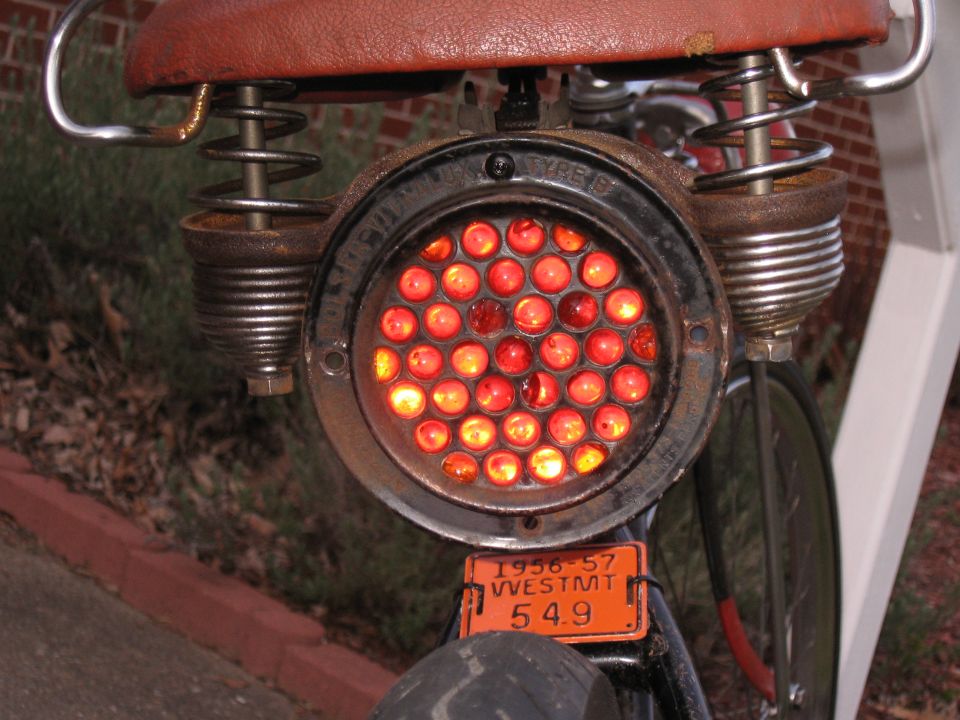 Bicycle tail light with red LEDs, rusty springs, and a 1956-57 license plate