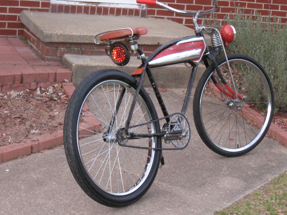 Old bicycle with red handlebars, a red headlight, and a red taillight. It has a chrome tank with red accents