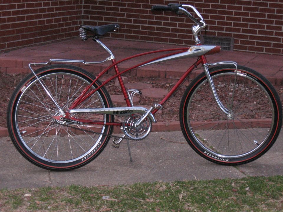 Red bicycle with chrome accents and black tires, parked on a sidewalk