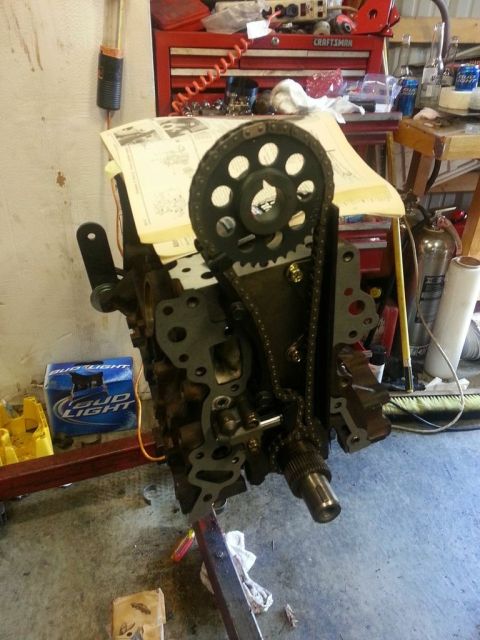 1987 Toyota 4Runner - Engine block with timing chain and gears, on an engine stand, with shop tools and manuals in background.
