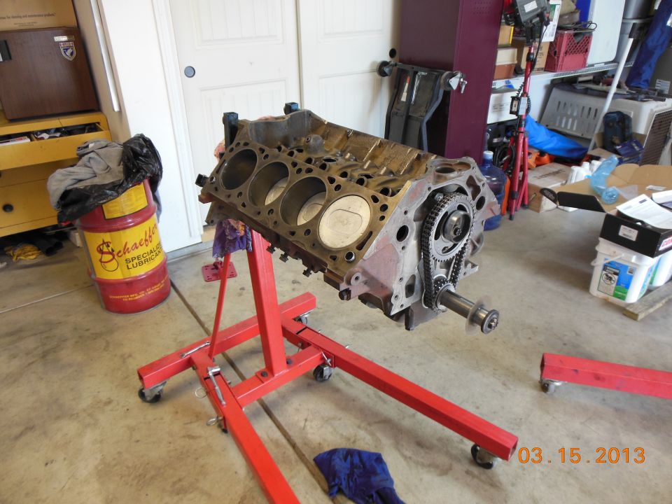 Engine block on red engine stand, with timing chain visible. Schaeffer's oil drum in background