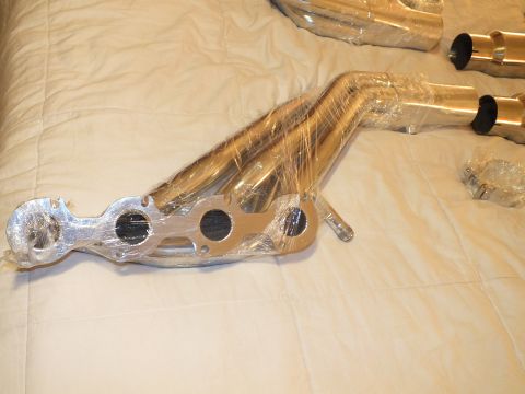 2003 Ford Crown Victoria - Close view of a plastic-wrapped polished tubular exhaust manifold header with three-port flange on a bedspread