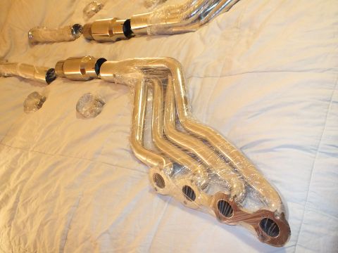2003 Ford Crown Victoria - Plastic-wrapped long-tube exhaust header with four runners beside two catalytic converters on a cream bedspread