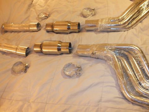 2003 Ford Crown Victoria - Polished catalytic converter canisters above plastic-wrapped header collector tubes and V-band clamps on a bed