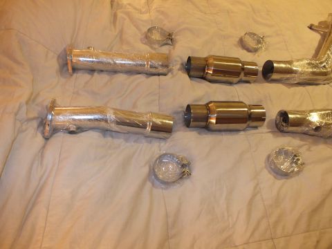 2003 Ford Crown Victoria - Multiple wrapped polished exhaust pipe sections, catalytic converters and round V-band clamps laid on a bed