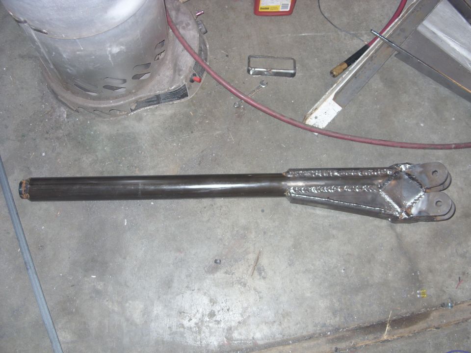 Metal suspension part with welded brackets and two mounting holes, lying on a concrete floor