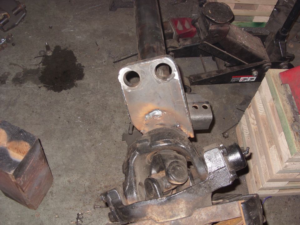 Close-up of a differential housing with a welded metal bracket attached. A driveshaft is visible