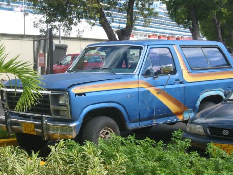 1992 Ford Bronco - This blue Ford Bronco has distinctive orange and yellow stripes on its side. Another car is parked next to it.