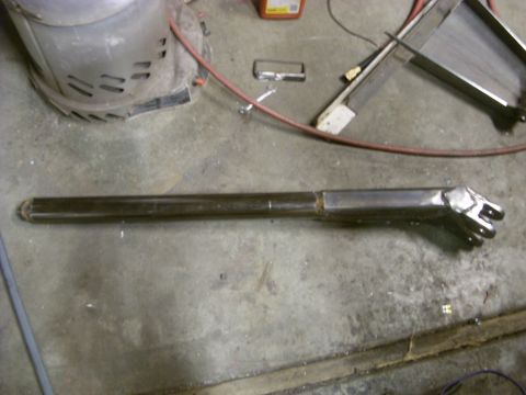 1967 Ford F-250 - A close-up view of a custom-made metal component, possibly a suspension or linkage part, lying on a workshop floor.
