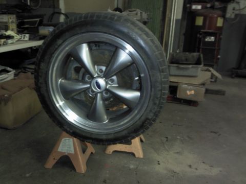 1967 Ford F-100 - A close-up of a Ford wheel and tire, resting on jack stands in a workshop environment.