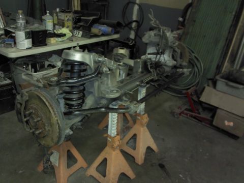 1967 Ford F-100 - A disassembled front suspension assembly is supported by orange jack stands in a workshop setting.