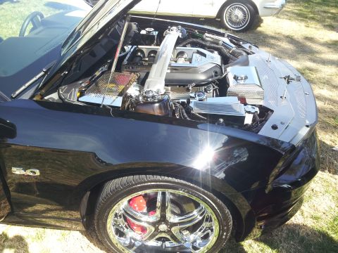 1965 Ford Mustang - The "5.0" badge on this black Ford Mustang indicates its engine size, with the hood open to reveal the engine compartment.