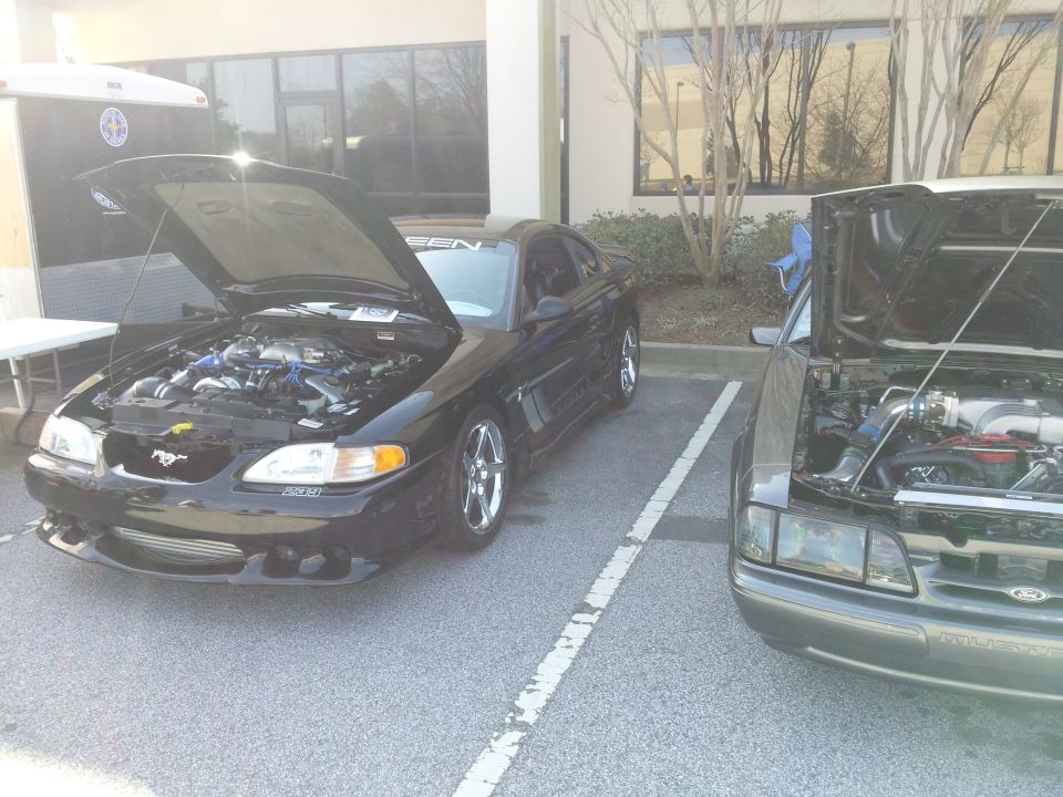 Two Ford Mustangs parked side-by-side, both with hoods open showing engines