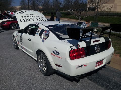 1965 Ford Mustang - This white racing Mustang features a large rear spoiler and an open hood, displaying sponsor decals.