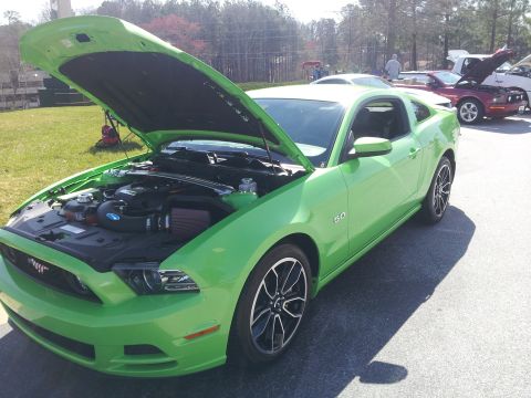 1965 Ford Mustang - A bright green Ford Mustang is displayed with its hood up, revealing the engine compartment. A "5.0" emblem is visible on the side.
