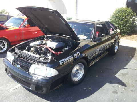 1965 Ford Mustang - This black police car, marked "Force 911" and "SHERIFF", is displayed with its hood open, showing the engine compartment.