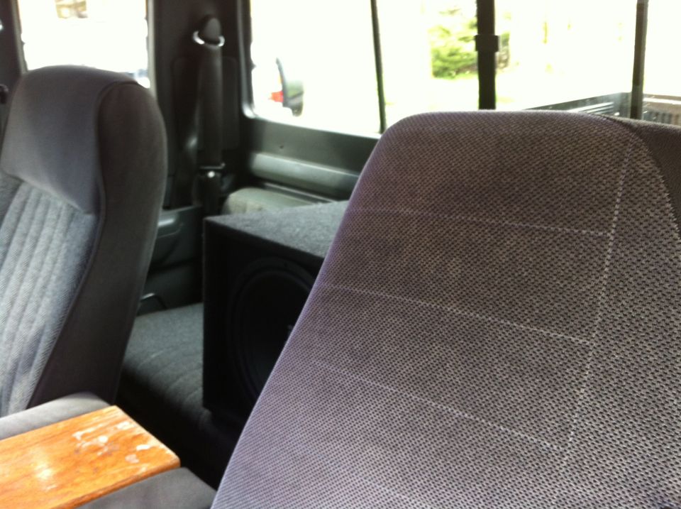 Interior view of a vehicle showing front seats and a subwoofer box behind them
