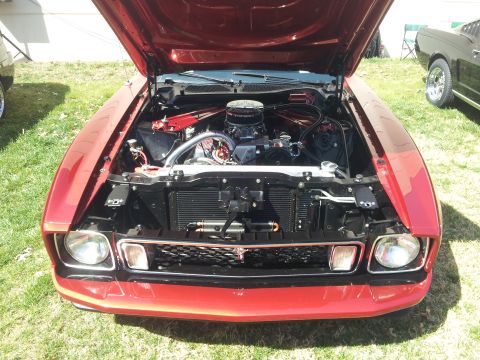 1965 Ford Mustang - The engine bay of a red 1971 Ford Mustang is open, revealing a modified engine with chrome accents and an aftermarket air cleaner. Another…